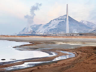 Scene of mountains and water with factories in the distance