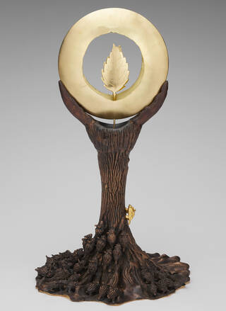 Sculpture in the shape of a tree with animals walking up the trunk and a gold disk with leaves in the centre at the top