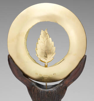 Gold circle with two gold leaves inside it. Hallmarks and makers marks visible on the bottom.