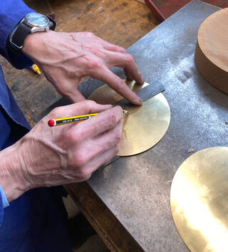 Hands holding a pencil and ruler, making a mark on a gold disk