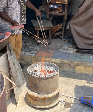 Arm holding tongs and metal pieces above small fire pit