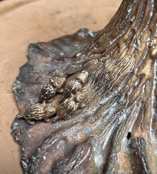 Four brown metal creatures on the base of a tree sculpture