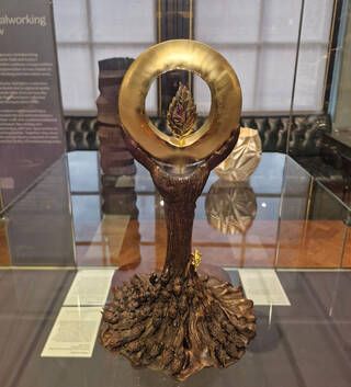 Gold and bronze sculpture of a tree and sun on display in a glass cabinet