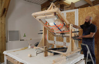 Man standing on a ladder tipping a mould upside down in a large wooden frame