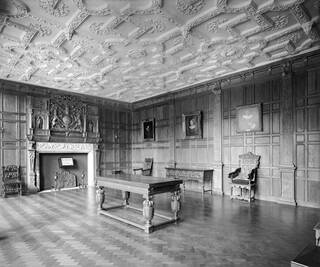 Black and white photograph of a room with panelled walls and decorative ceiling