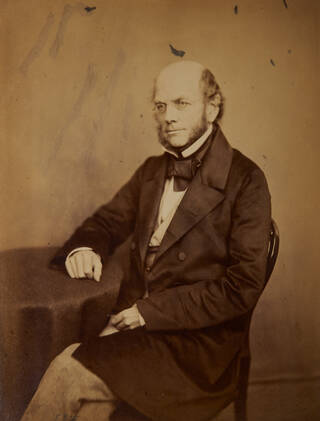Sepia-toned photograph of a seated man with right arm resting on a table