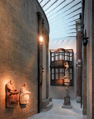 Photograph of a brightly lit sculpture gallery with large wooden staircase