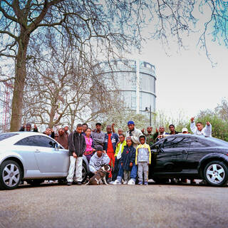 Photo of a group of people posing in the road between two cars