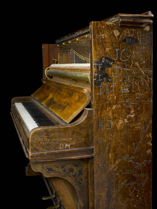 Side view of a piano covered in scratched graffiti 