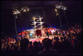 Photograph of acrobats stacked up on poles in a big top circus tent