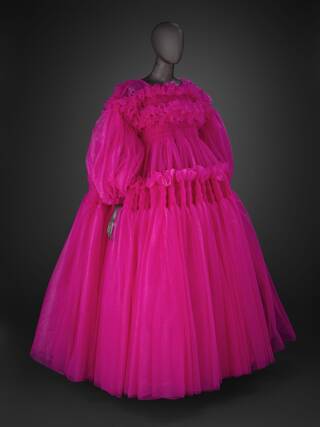 A pink chiffon dress with ruffles created by smocking on the bodice and skirt which frame the wide, off-the-shoulder neckline