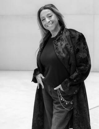 Black and white photo of a woman in a long, dark jacket and jeans with her hands in her jean pockets
