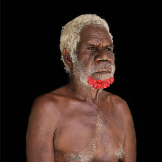 Photograph of a bare-chested Black man turned side-on to the camera with his beard decorated with pink flowers