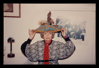 Photo of a woman facing the camera in a black, white and red top, wearing a large brimmed hat decorated with sea creatures