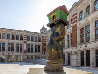 monumental sculpture of a figure with a house on its head in a courtyard setting