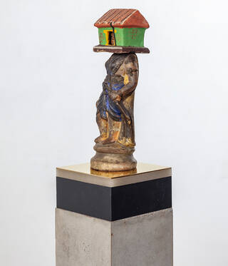 small sculpture of a figure with house on its head on a grey and black plinth