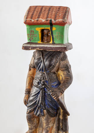 Detail of a sculpture with a green and red house on its head