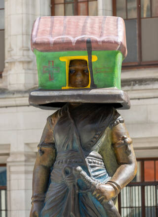 Detail of a sculpture of a figure with a red and green house on its head