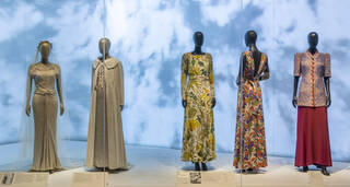 Five fashion ensembles on mannequins against a blue sky and cloud background