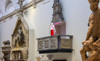 red and white costumed mannequin on a balcony surrounded by sculptures