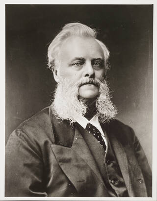 Black and white portrait photograph of a man with very long and bushy mutton chop facial hair
